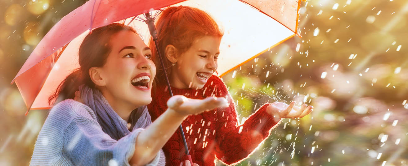 Mother and daughter sheltering under an umbrella on a sunny and rainy day.